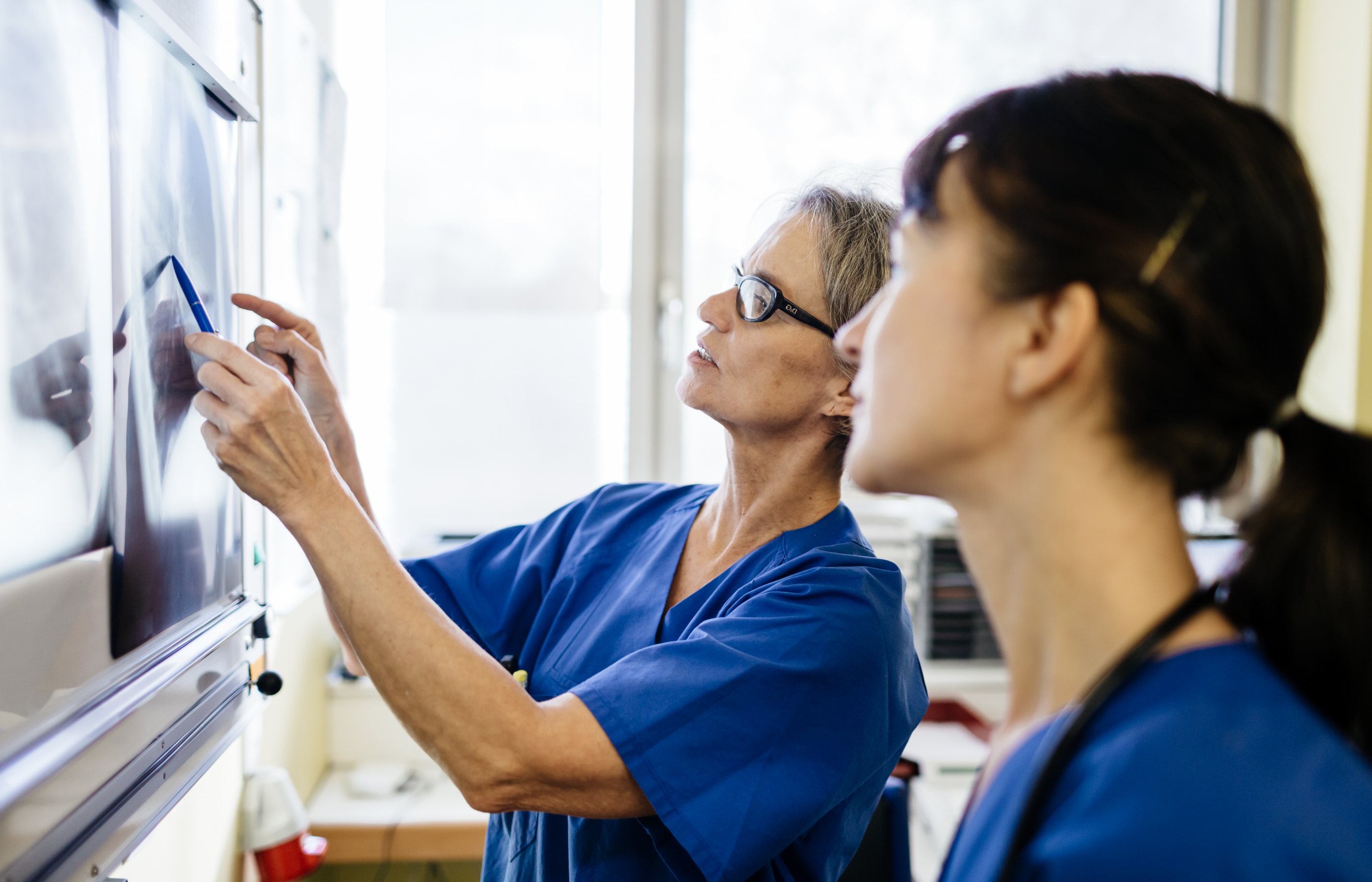 One team member is holding up and x-ray while pointing out some of the details. Another team member is standing alongside her discussing the imaging results. 
