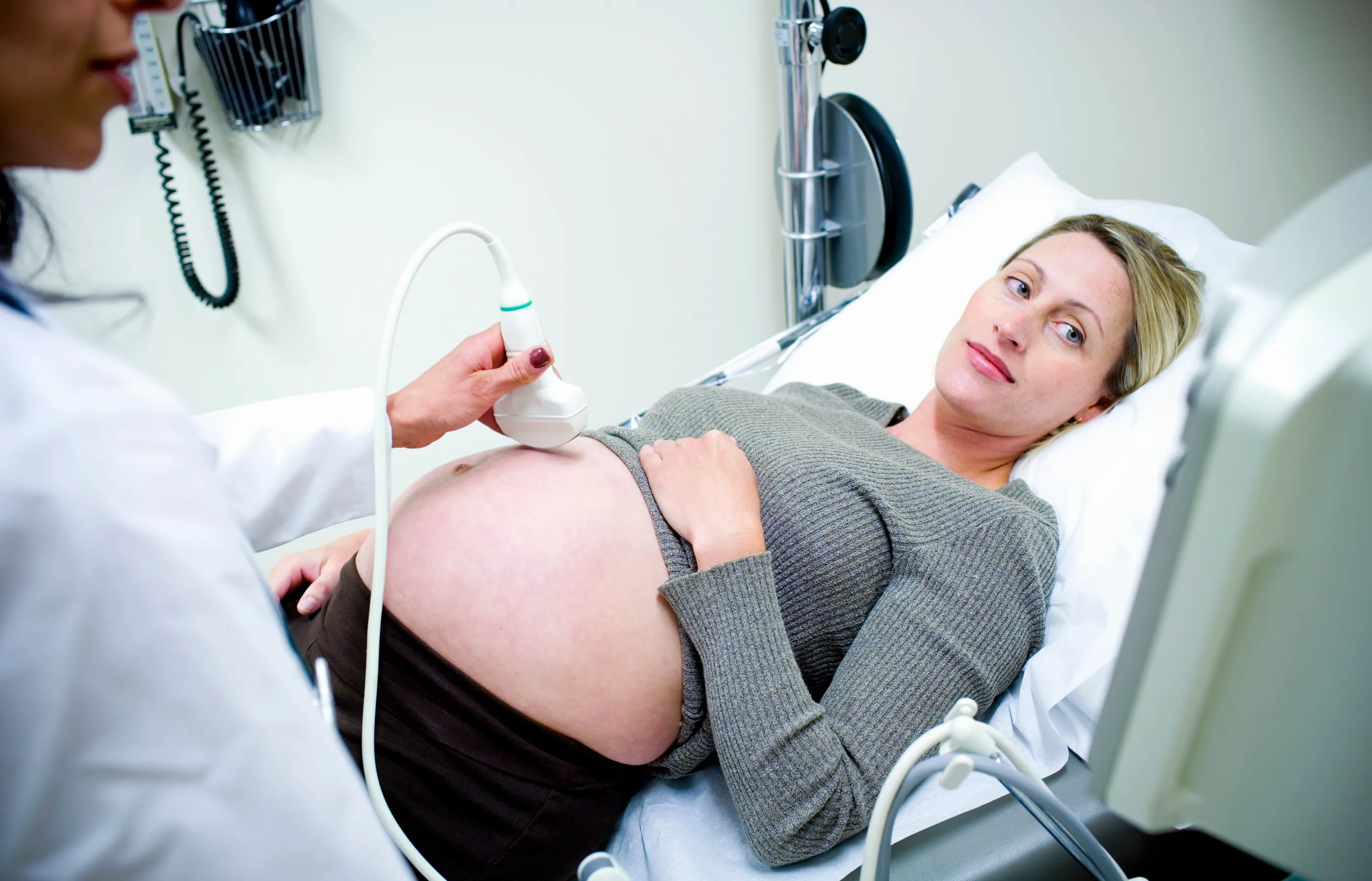 A woman is lying down on a clinic exam table as a team member performs and ultrasound.