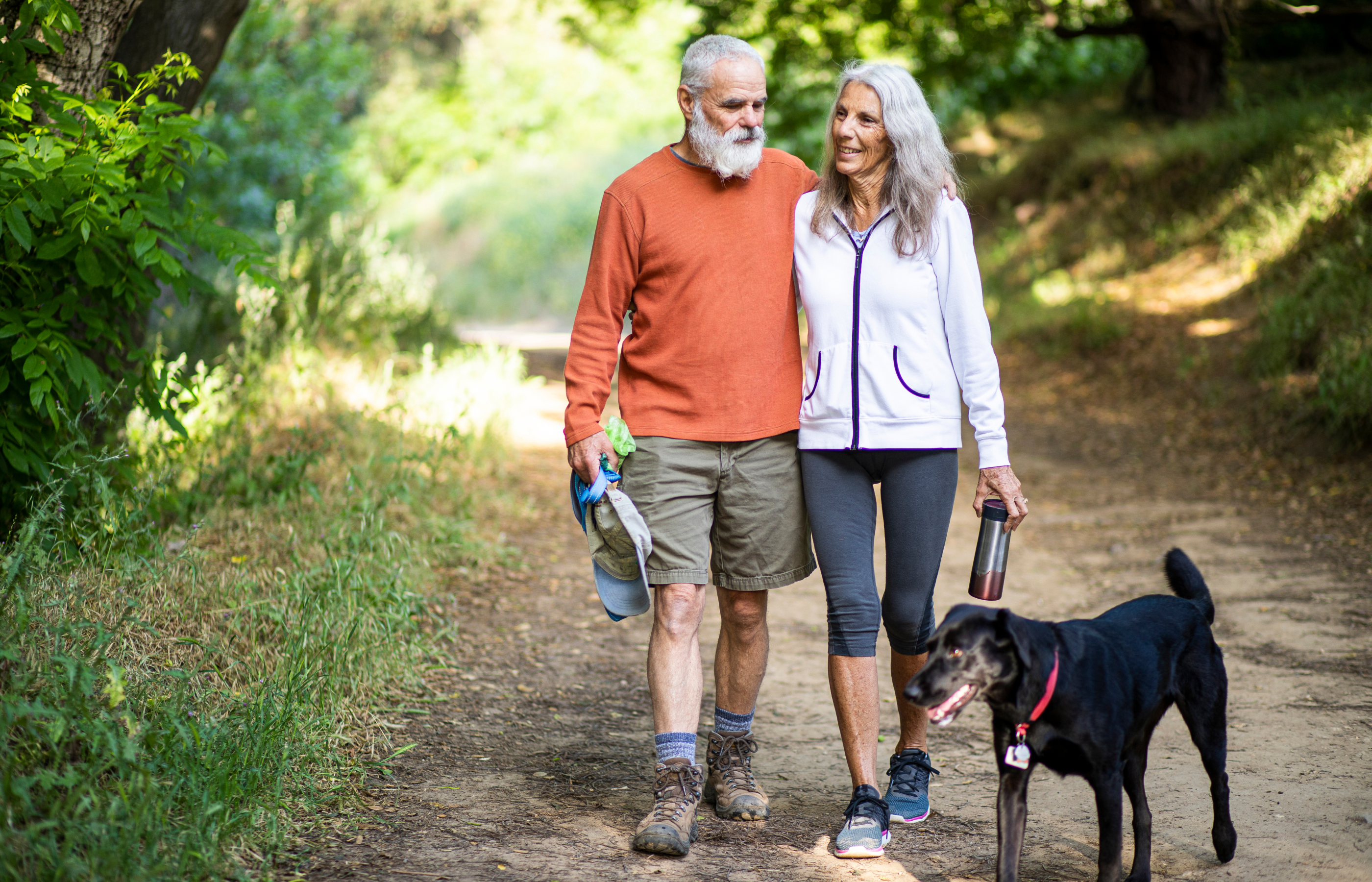 A man, a woman and a dog walking on a trail outdoors.
