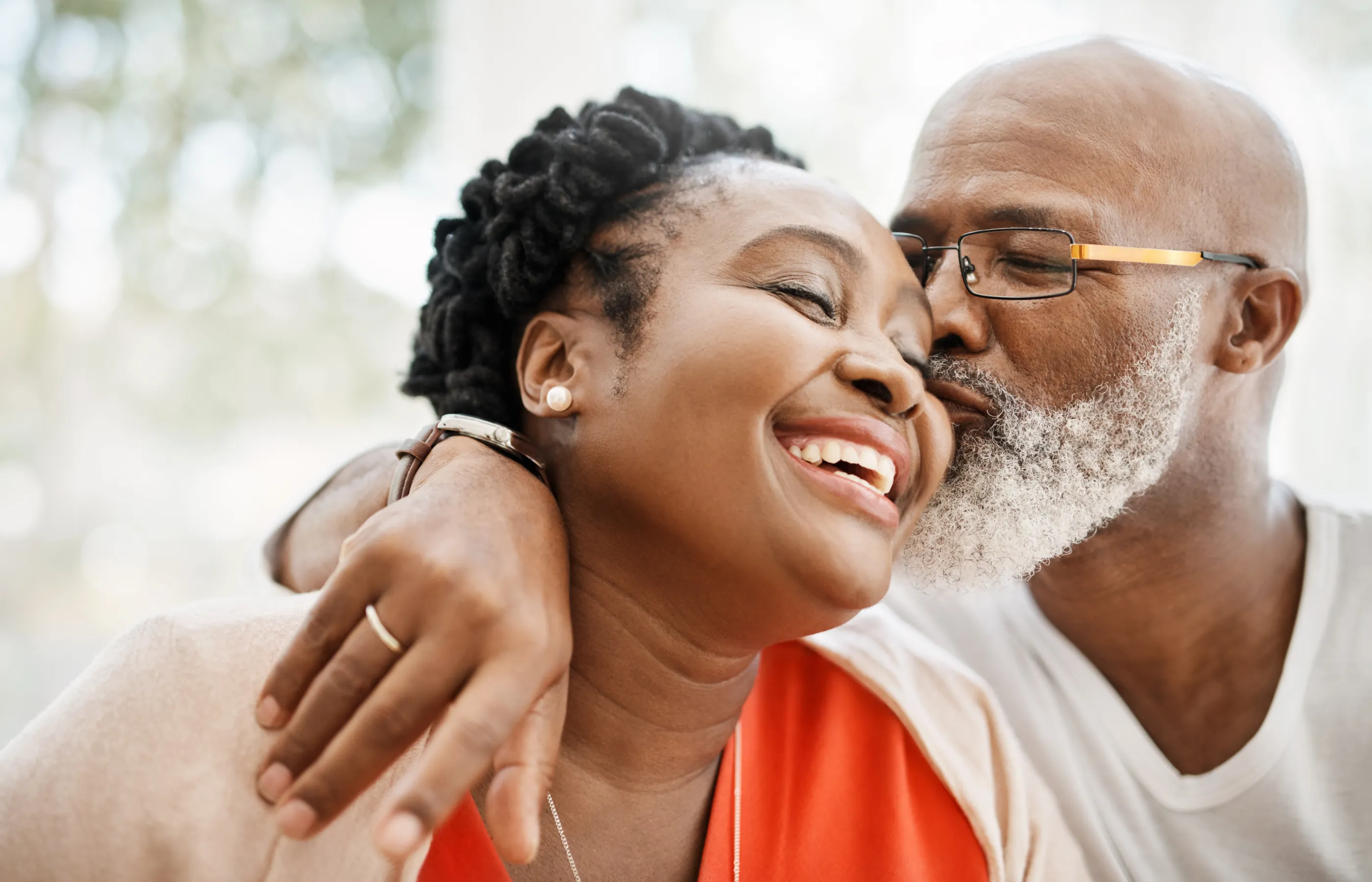 A man is hugging and kissing his partner on the cheek as she smiles. A man is hugging and kissing his partner on the cheek as she smiles.