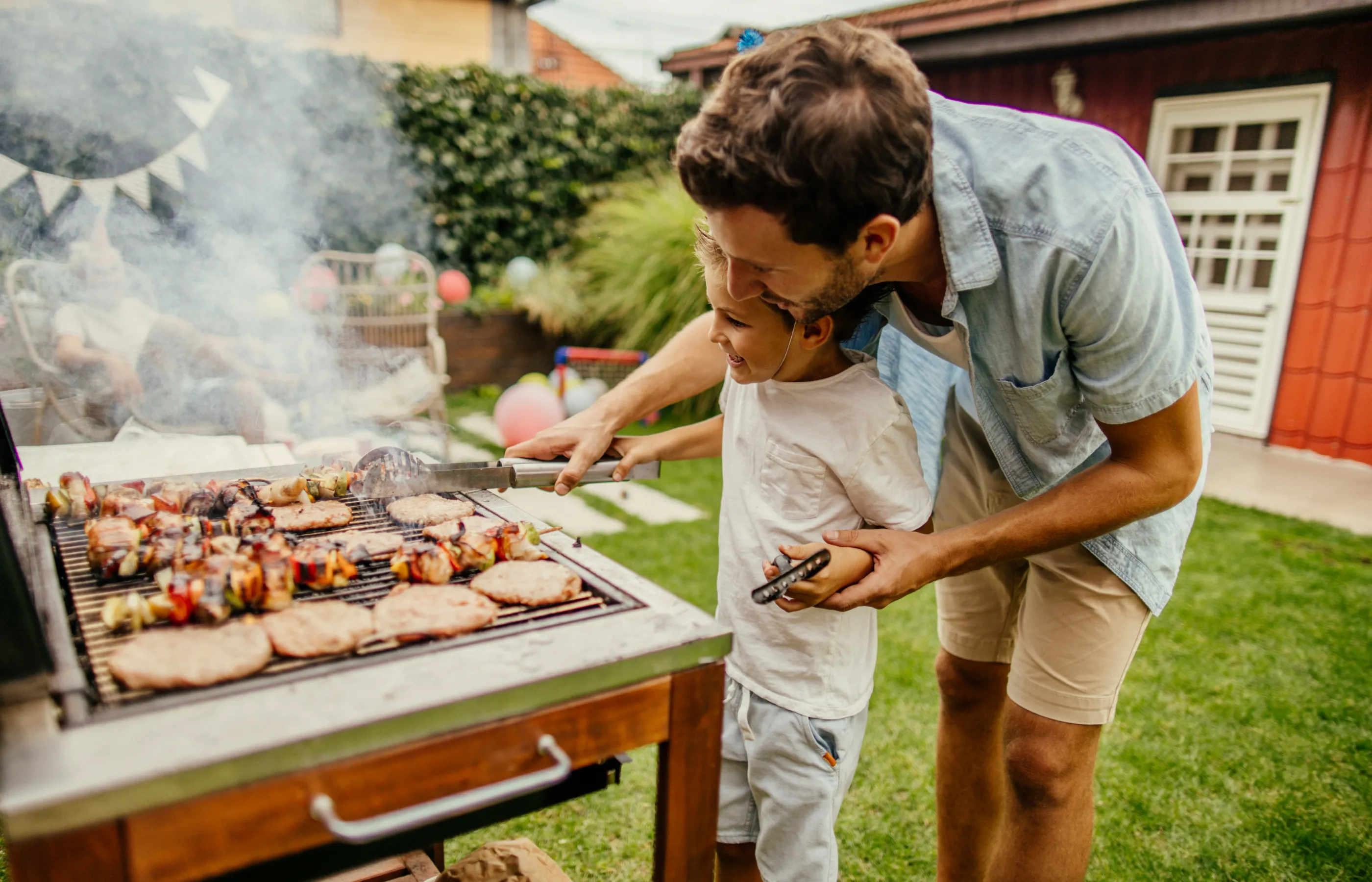 father and son grilling meat during the barbecue party in their yard
