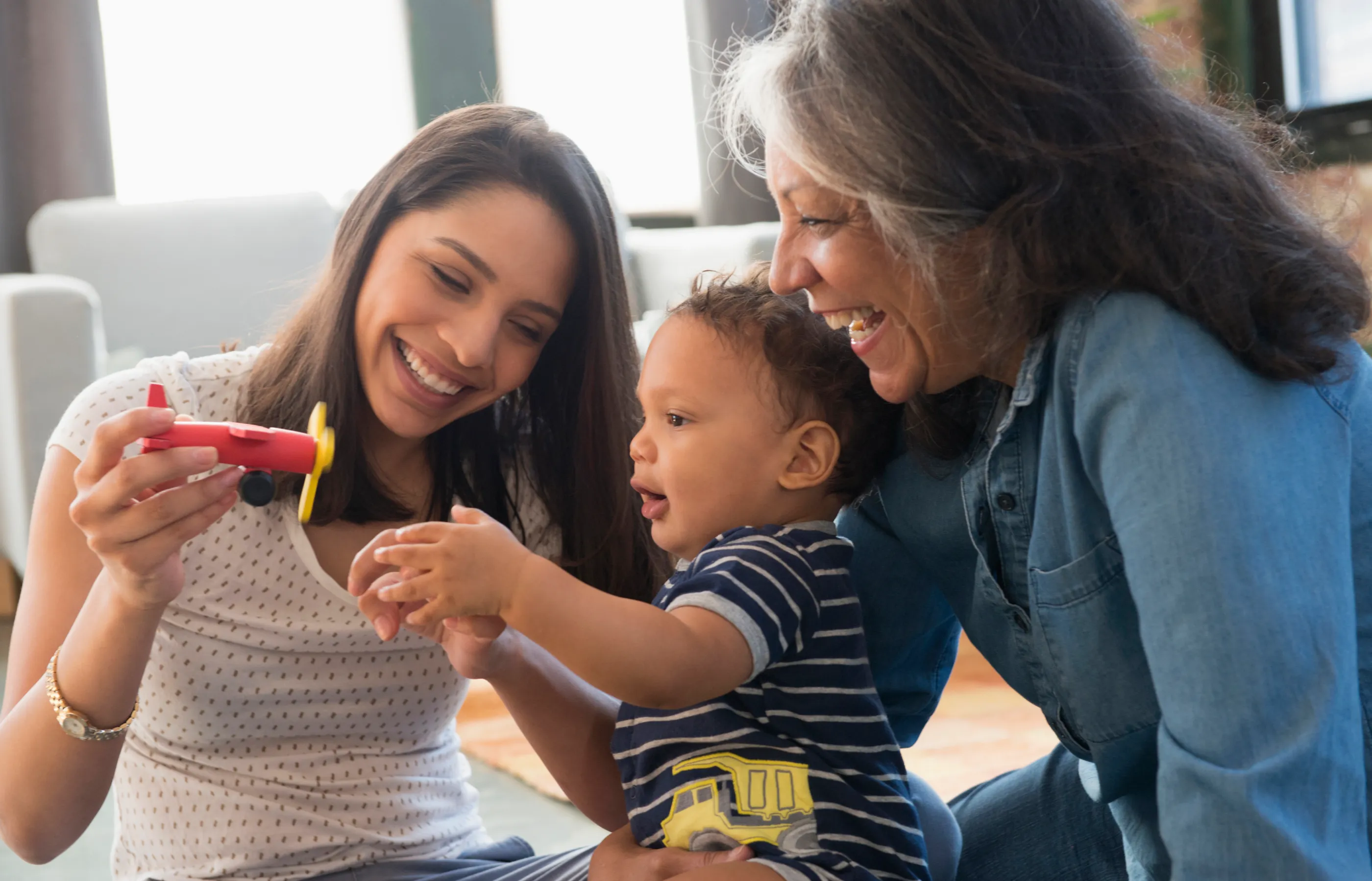 Grandmother, daughter and grandchild playing with toy airplane.