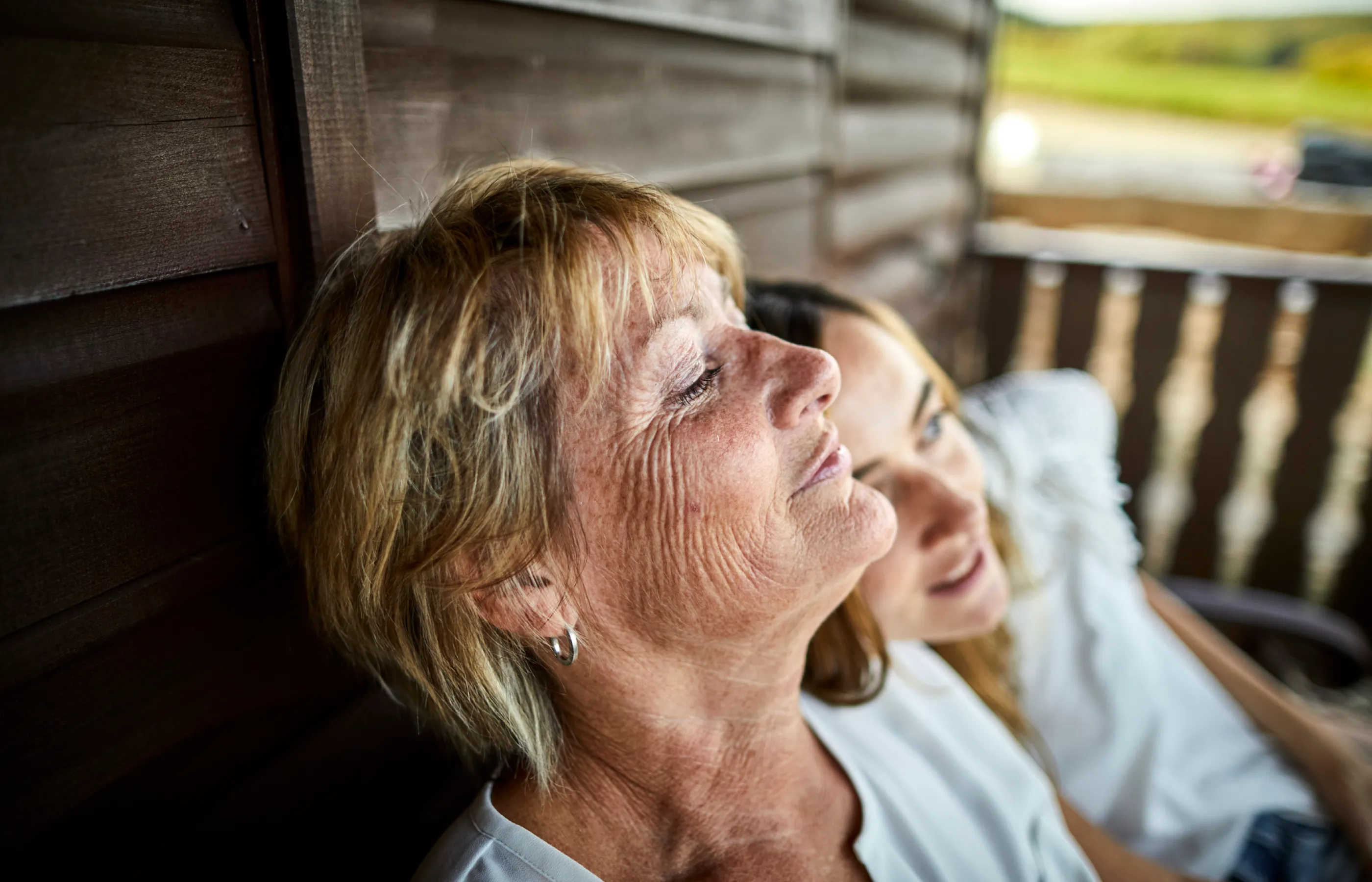 Adult mother and daughter sitting outside on a porch.