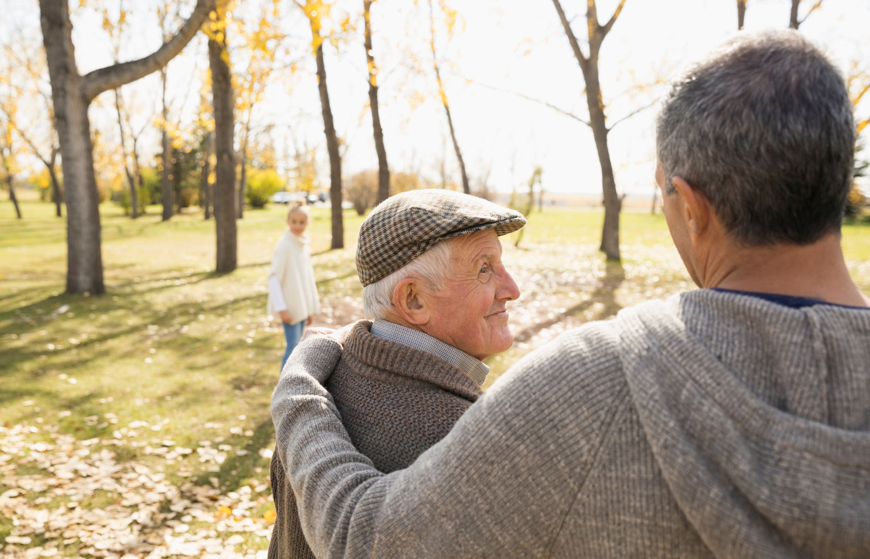 An elderly man in a newsbook cap smiles in a park with his family