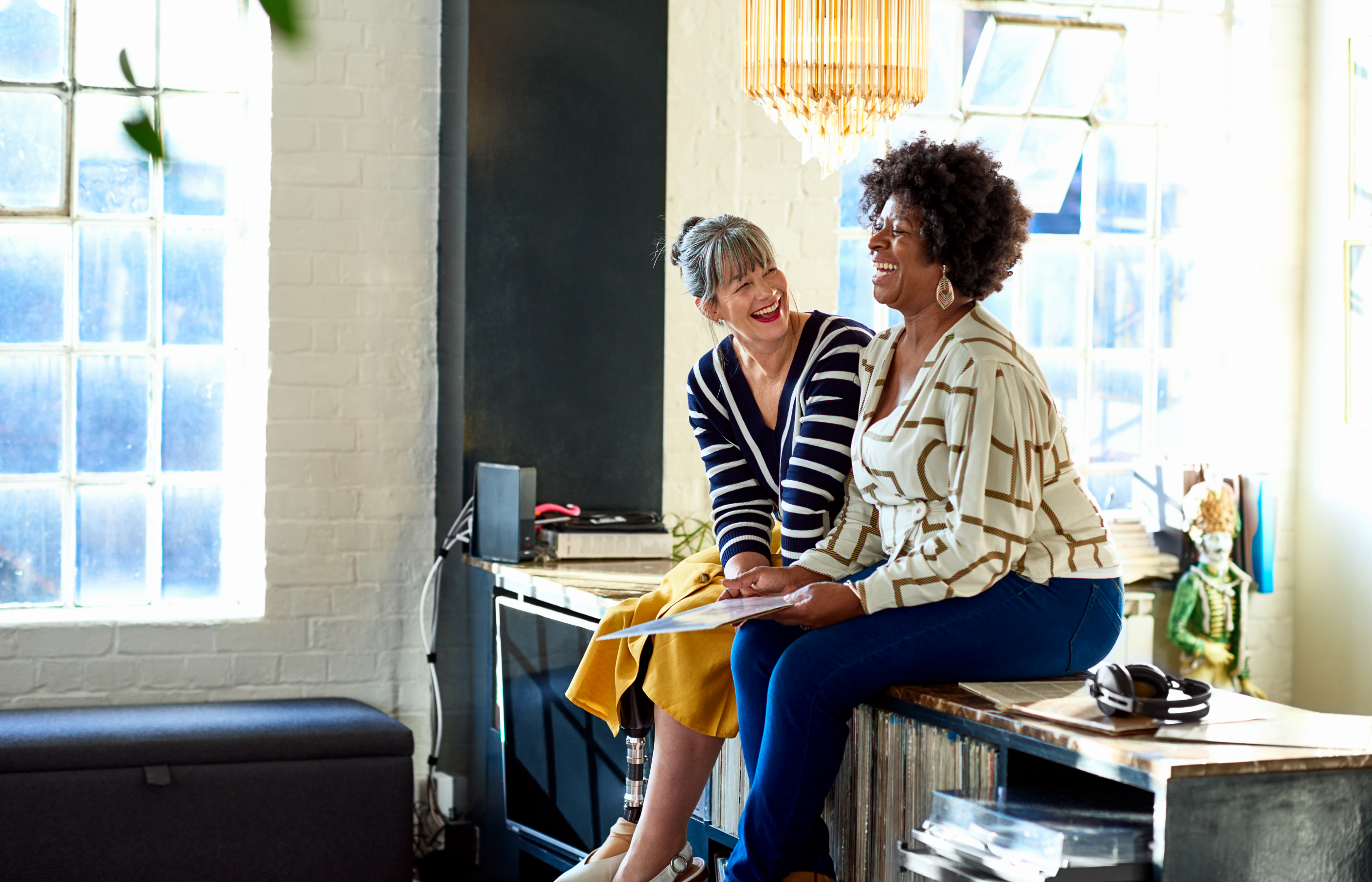 Two women sitting on a desk laughing. 