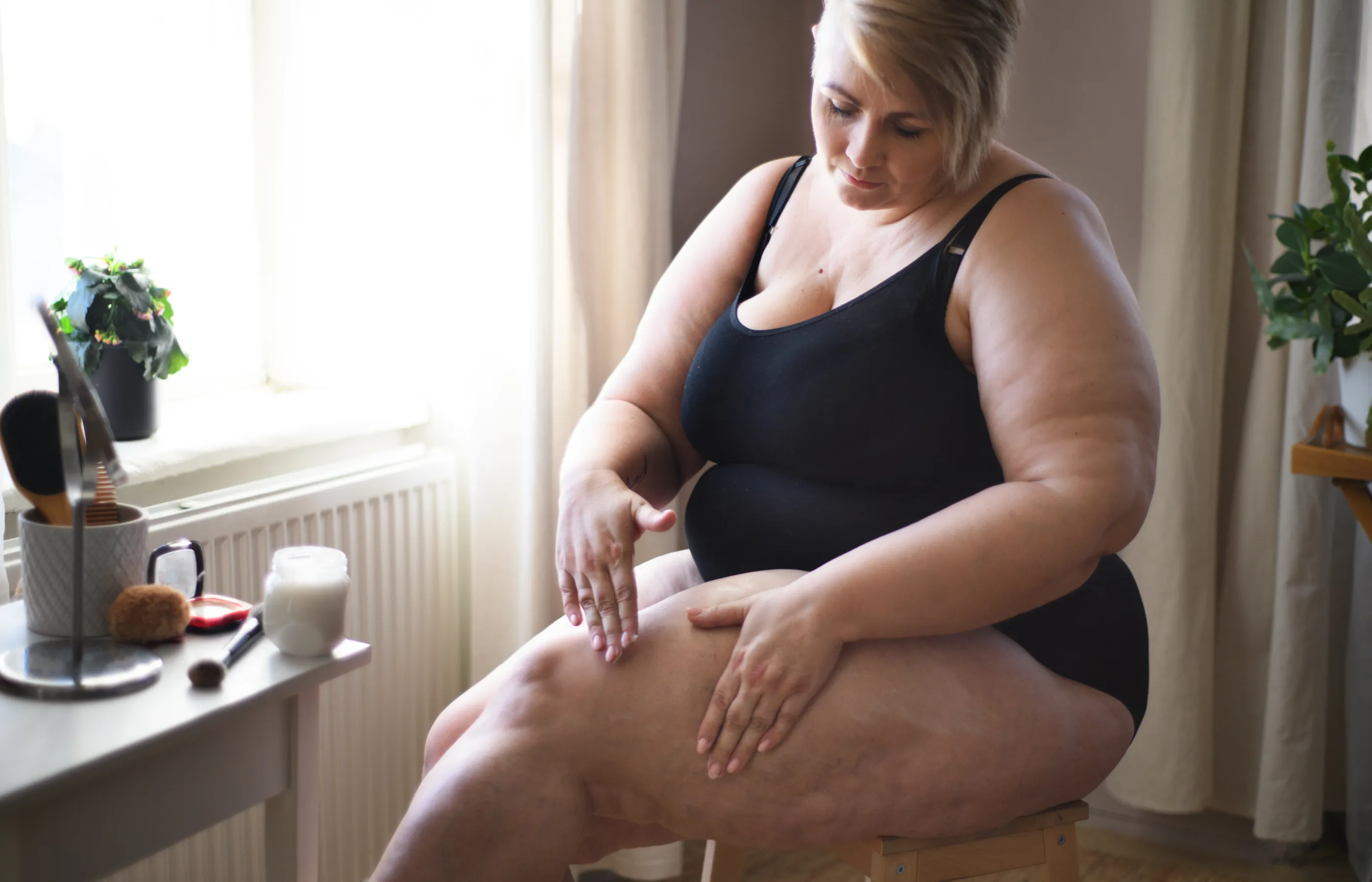 A woman is sitting in her home putting lotion on