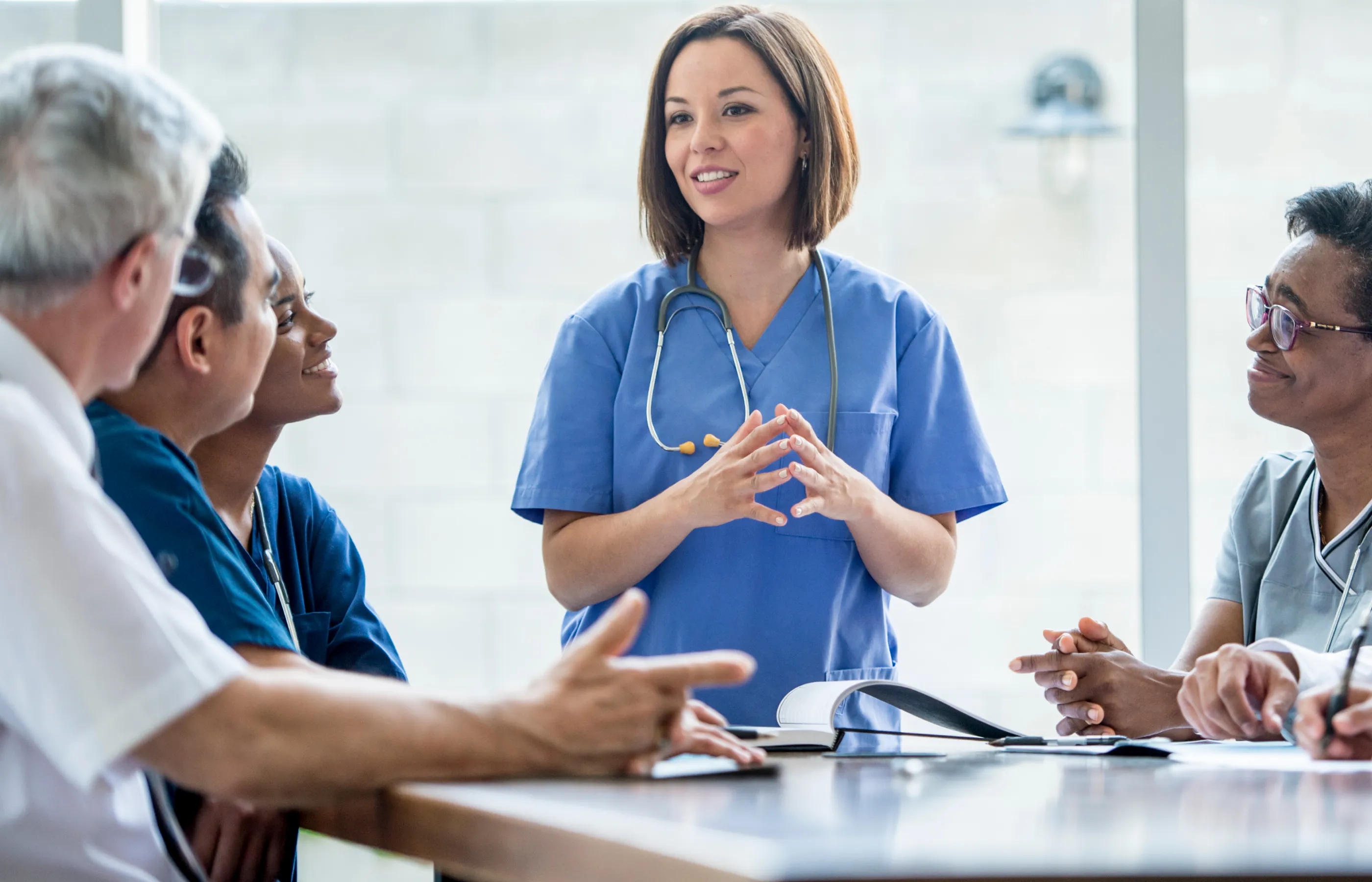 A group of residents are sitting around a table, wearing scrubs, talking.