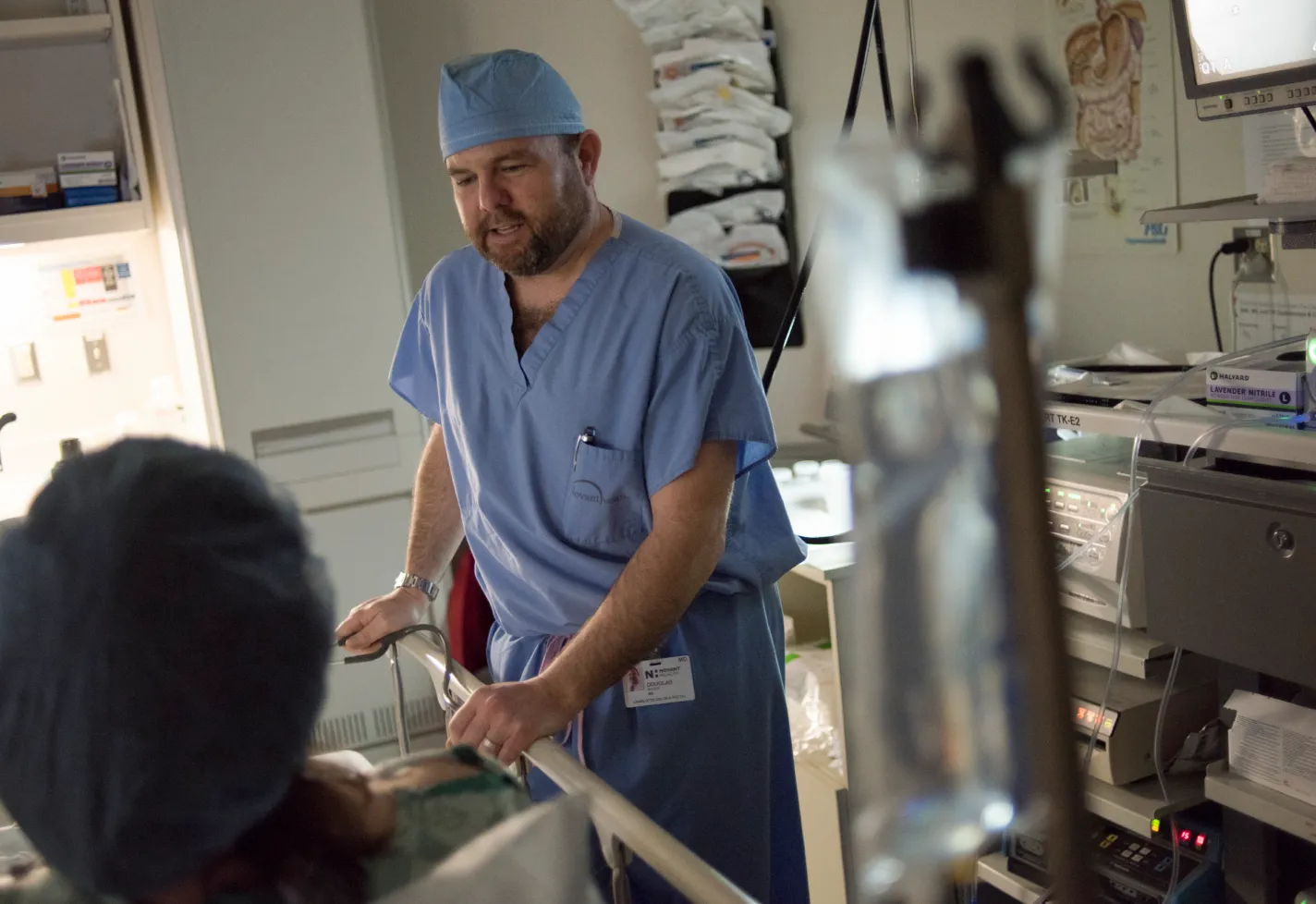 Novant Health's Dr. Douglas is standing at a patient's bedside, talking as they prepare for surgery. Novant Health's Dr. Douglas is standing at a patient's bedside, talking as they prepare for surgery.