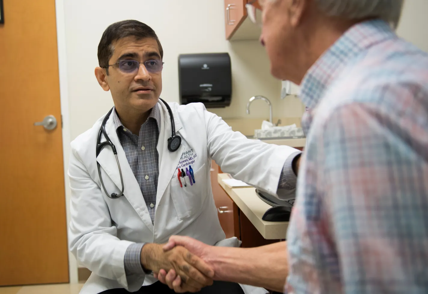 Dr. Tejwani is sitting across from a senior male patient in exam room. The two are shaking hands. Dr. Tejwani is sitting across from a senior male patient in exam room. The two are shaking hands.