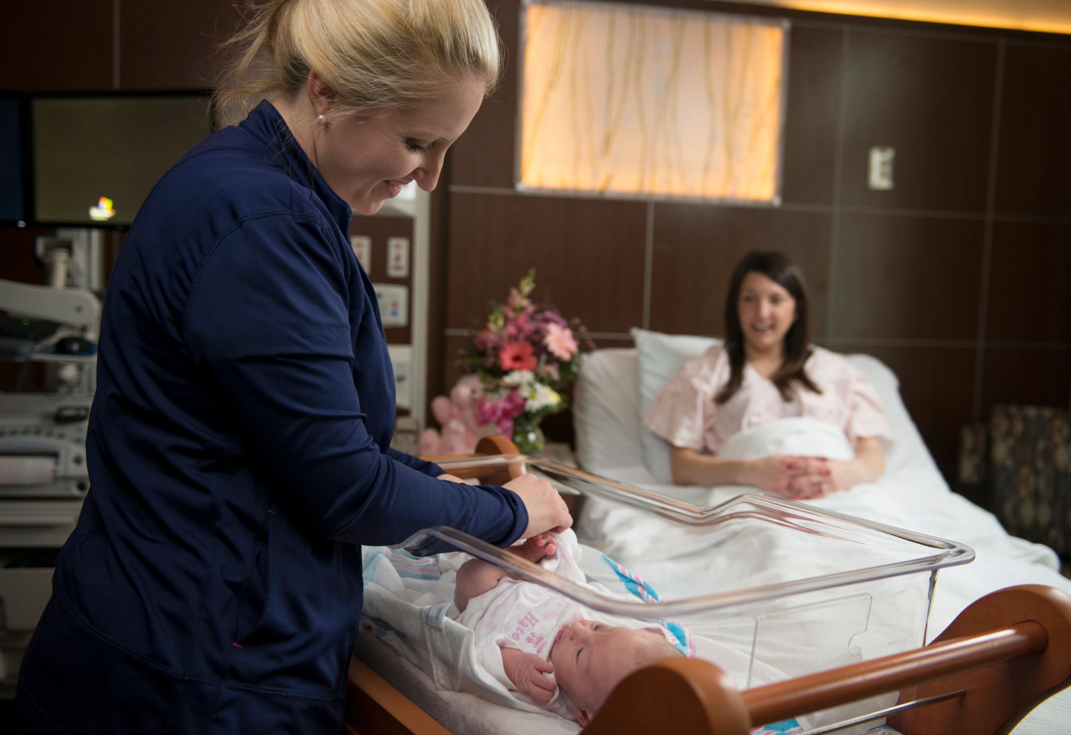 Novant Health nurse tends newborn in bassinet while mom smiles from bed Novant Health nurse tends newborn in bassinet while mom smiles from bed