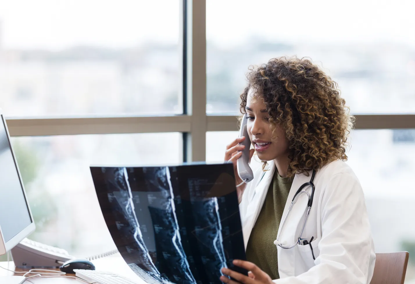 A health care provider is reviewing an x-ray while talking on the phone. A health care provider is reviewing an x-ray while talking on the phone.