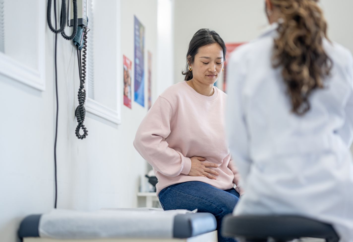 A female patient holds her side while a female doctor exams her.