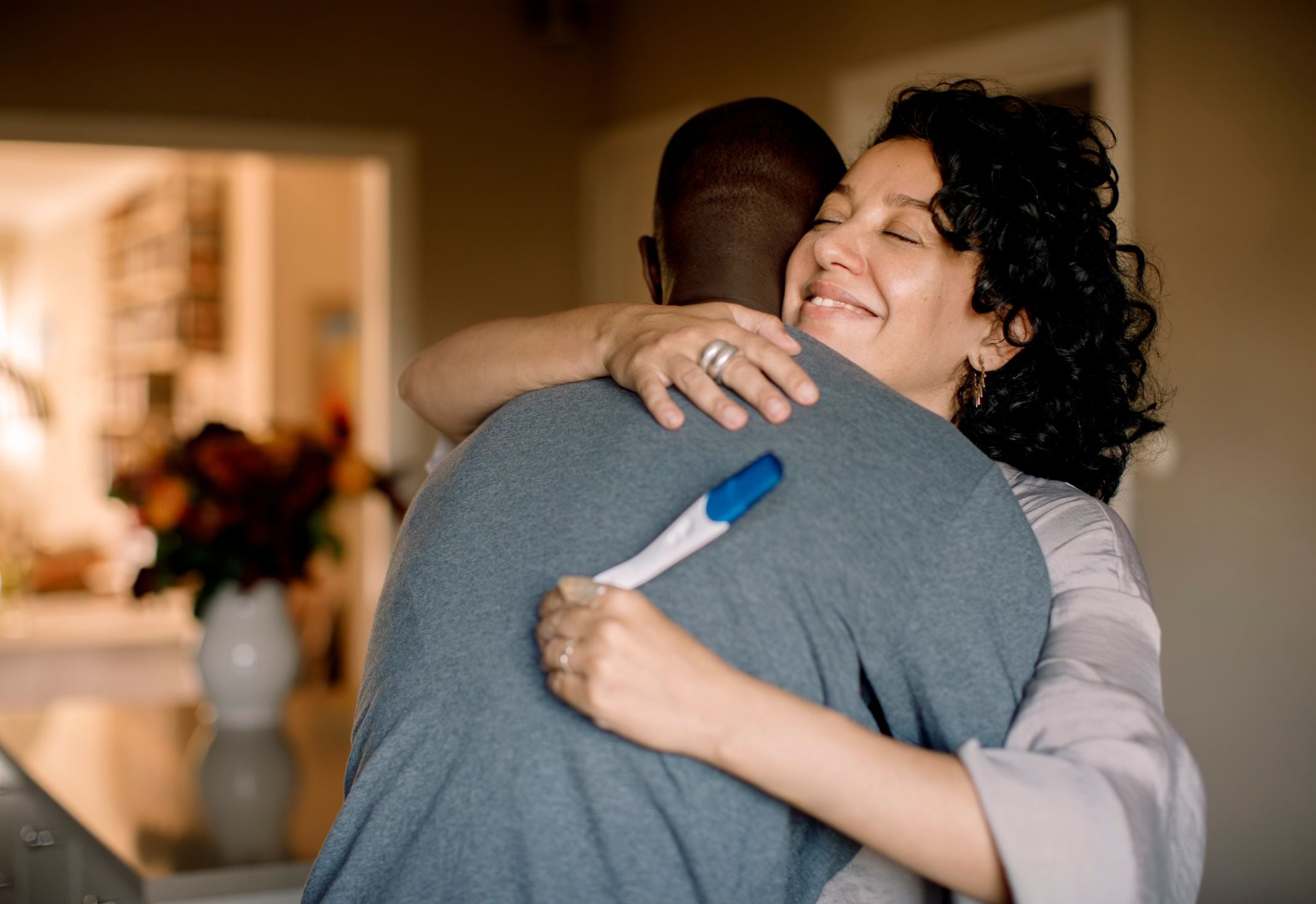 A couple holding a pregnancy test shares a smiling embrace.