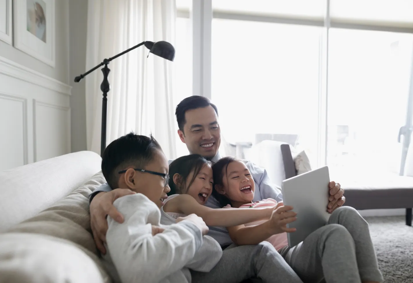 A father is sitting on a couch with his children on a video call. A father is sitting on a couch with his children on a video call.