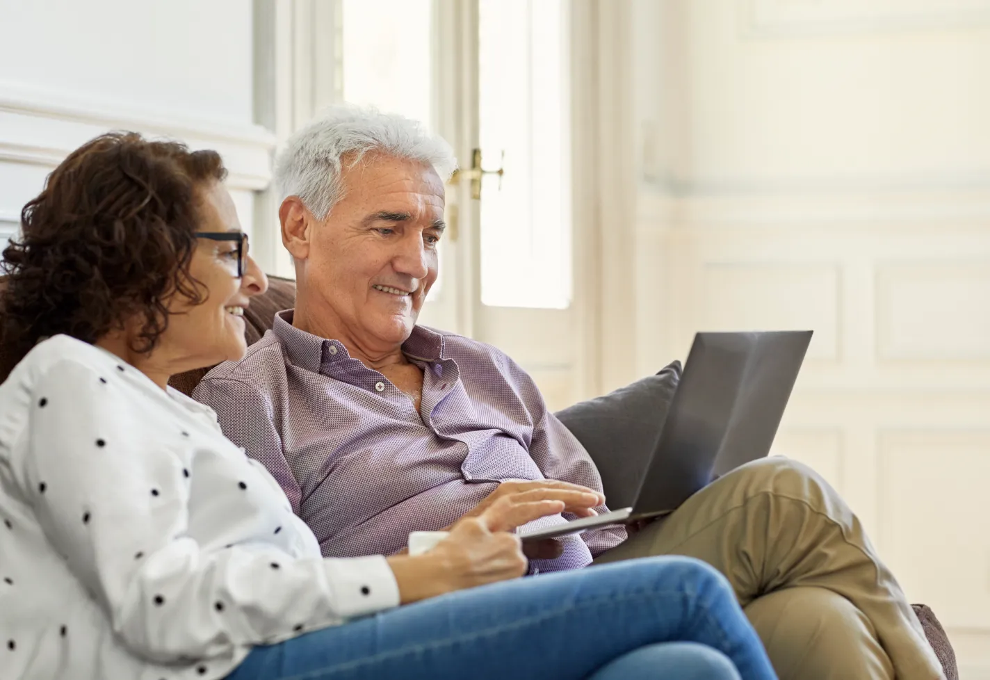 Senior couple sitting in their home reviewing information on a laptop. Senior couple sitting in their home reviewing information on a laptop.