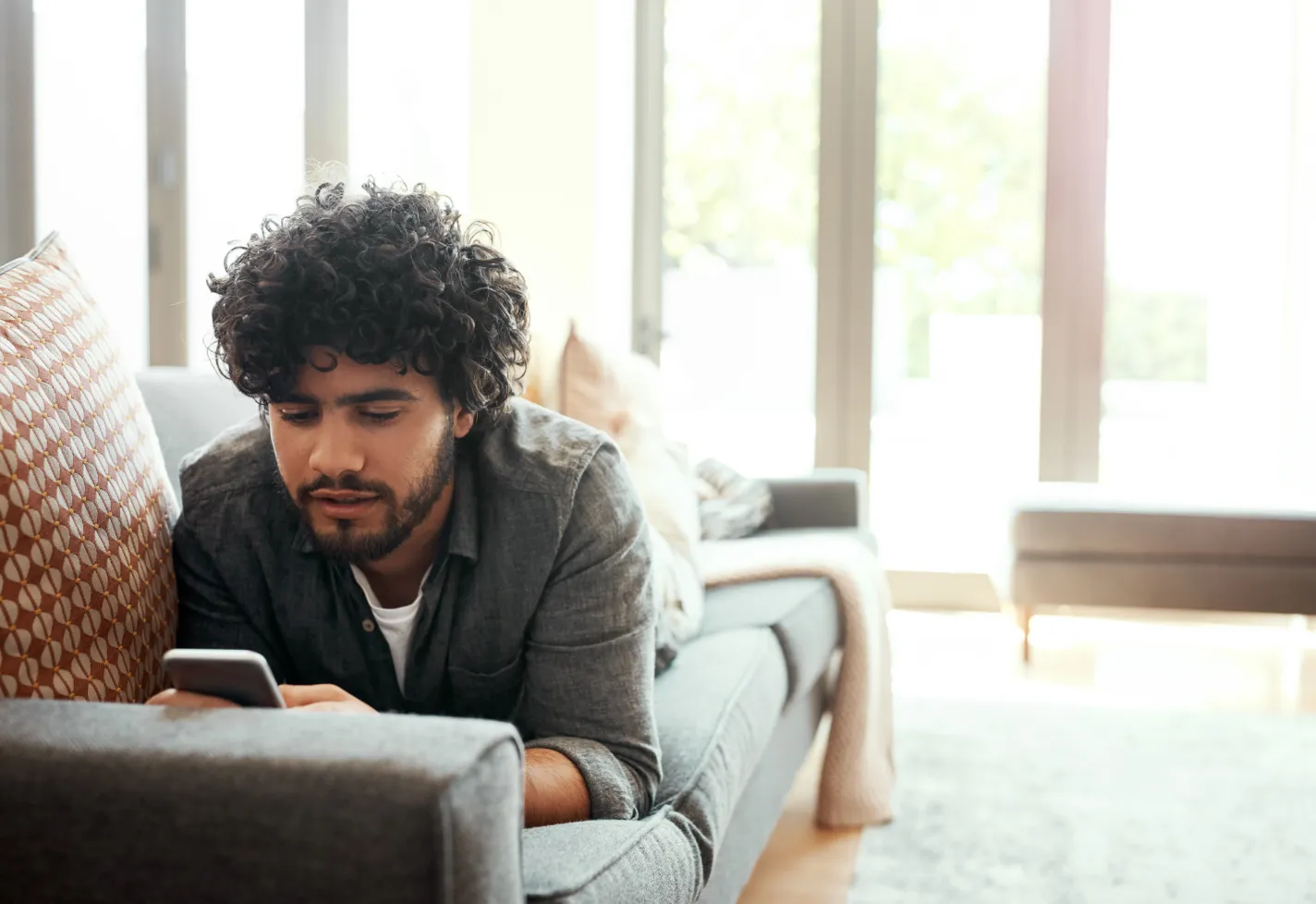 A young man is looking at information on his smartphone as he is lying down on a couch. A young man is looking at information on his smartphone as he is lying down on a couch.