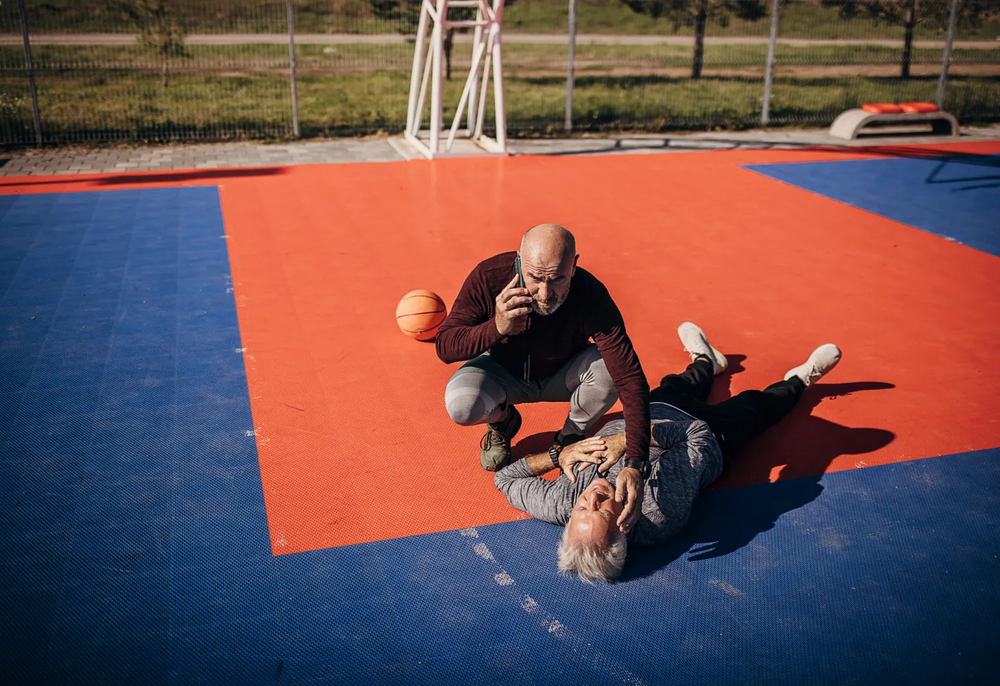 Senior man having a heart attack on sports court outdoors while his friend calls an ambulance. Senior man having a heart attack on sports court outdoors while his friend calls an ambulance.