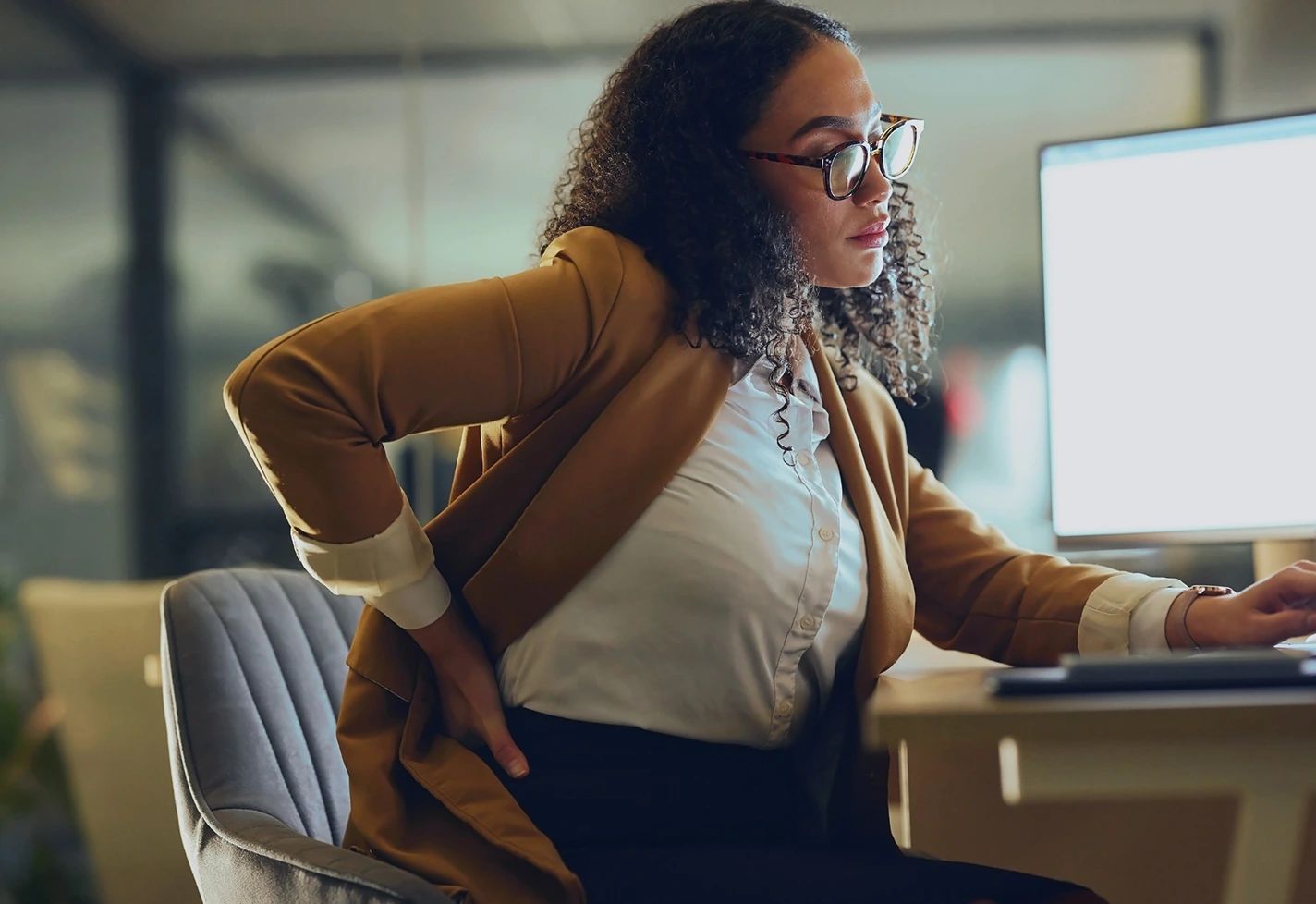 A professional woman in business attire and glasses looking at a computer screen.