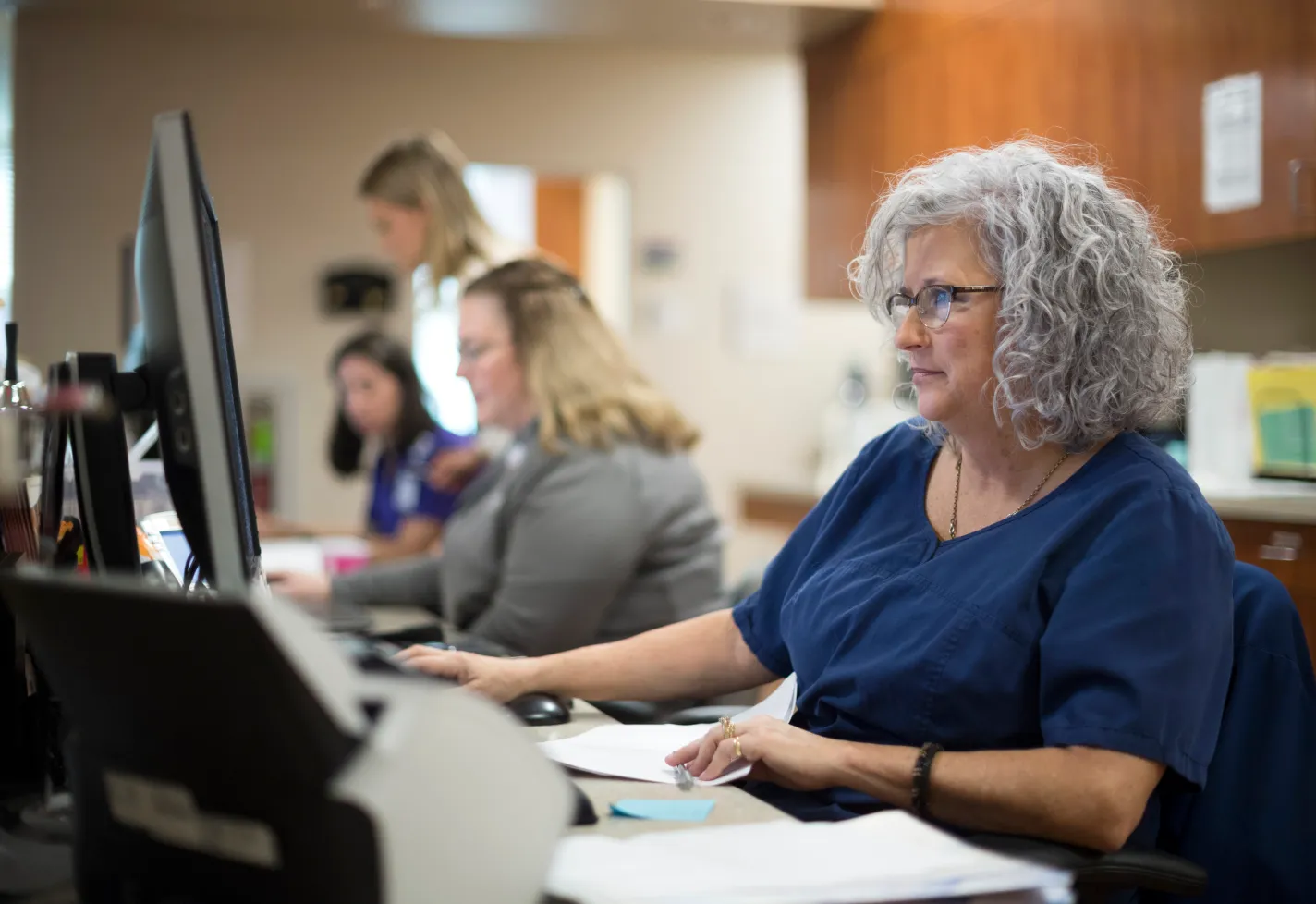 Woman team members in a clinic office reviewing patient information on computer screens