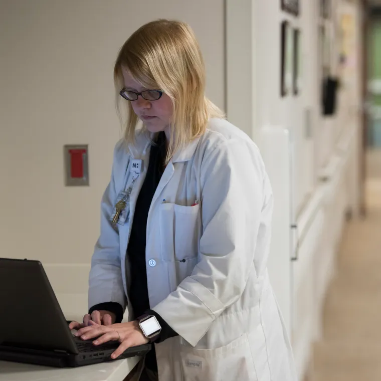 A Novant Health doctor is standing in a hallway typing on a laptop. A Novant Health doctor is standing in a hallway typing on a laptop.
